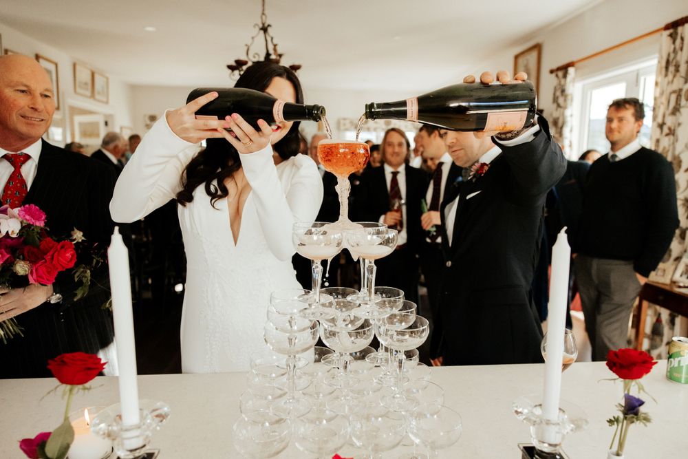 Wedding guests participate in a champagne tower pouring celebration indoors.