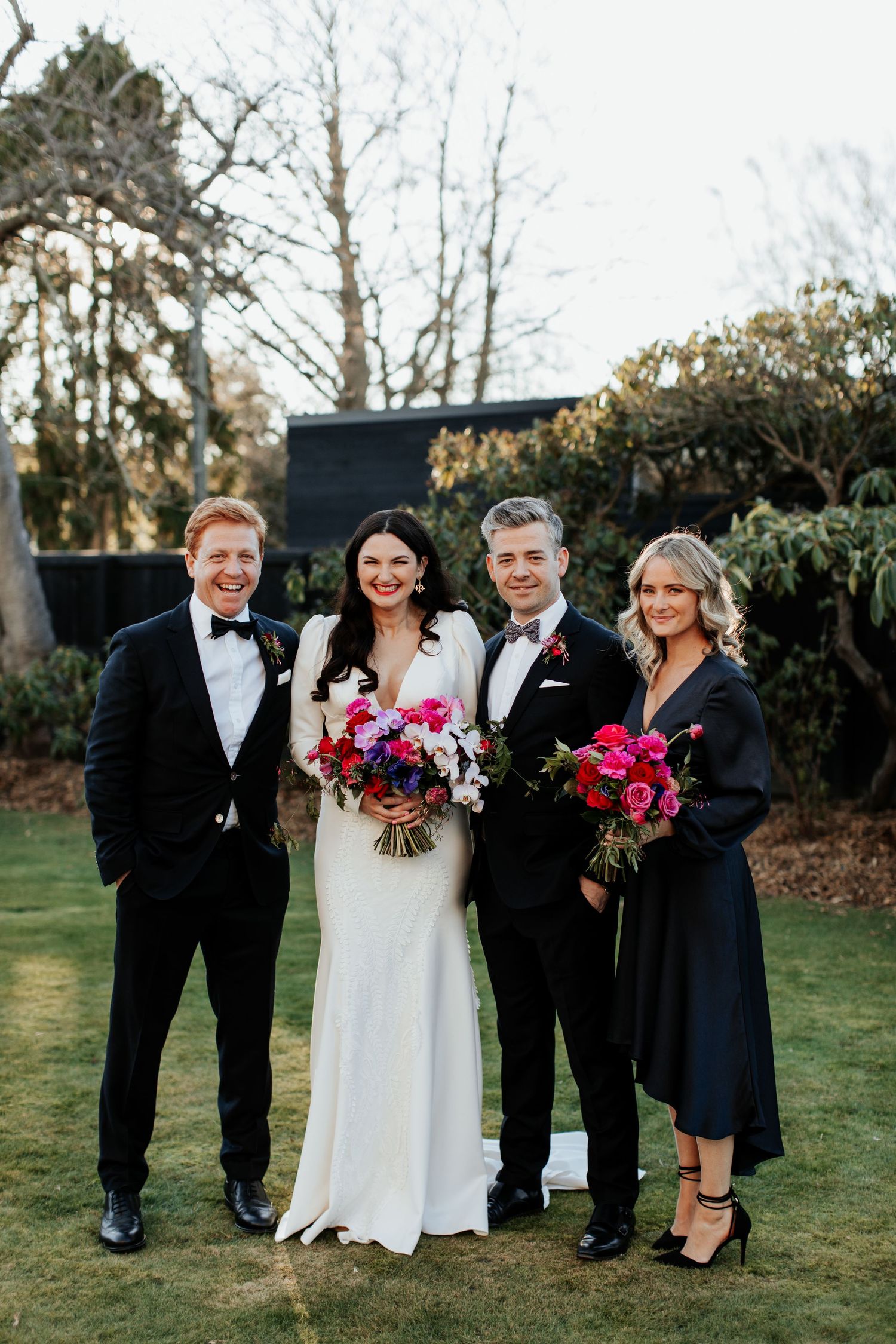 A wedding party poses on a lawn with vibrant pink bouquets and formal attire.