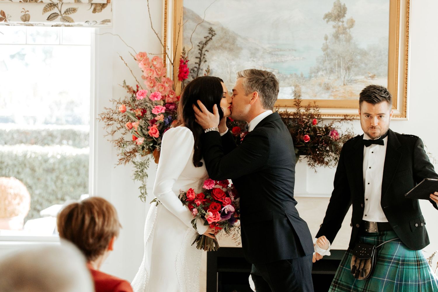 Wedding ceremony moment with red and pink floral arrangements decorating the intimate indoor space.
