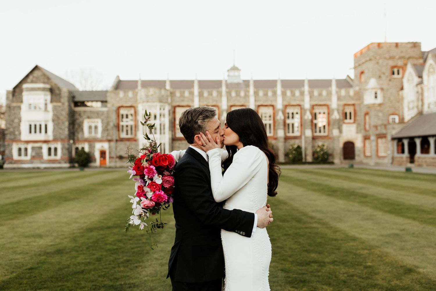 A romantic moment captured on the lawn of a grand Gothic revival building with pink florals.