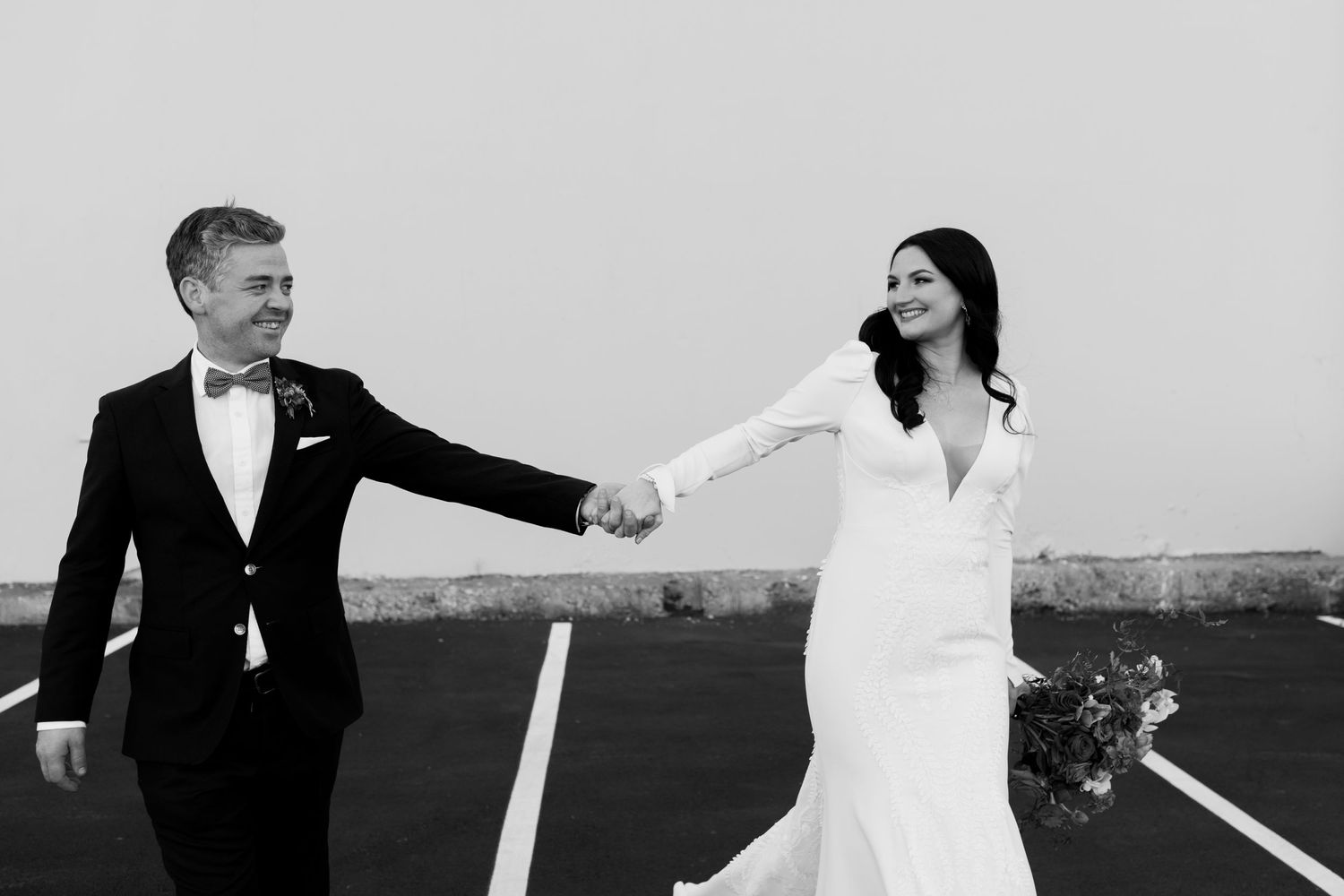 Black and white image of couple reaching toward each other across parking lot lines.