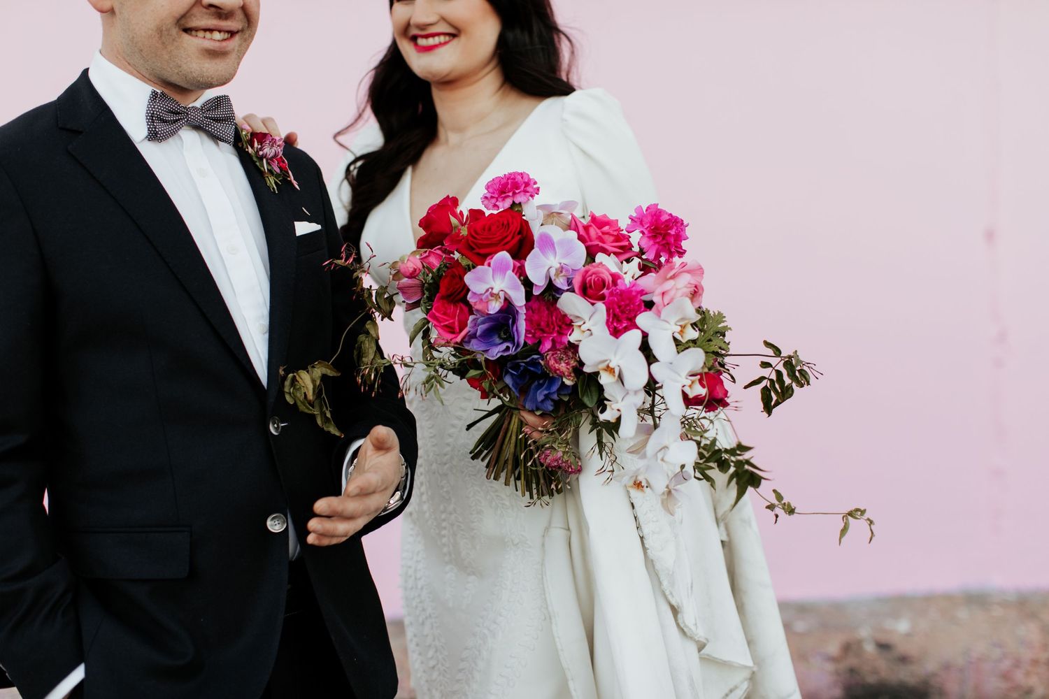 Close-up of couple with vibrant pink bouquet against soft pink wall.