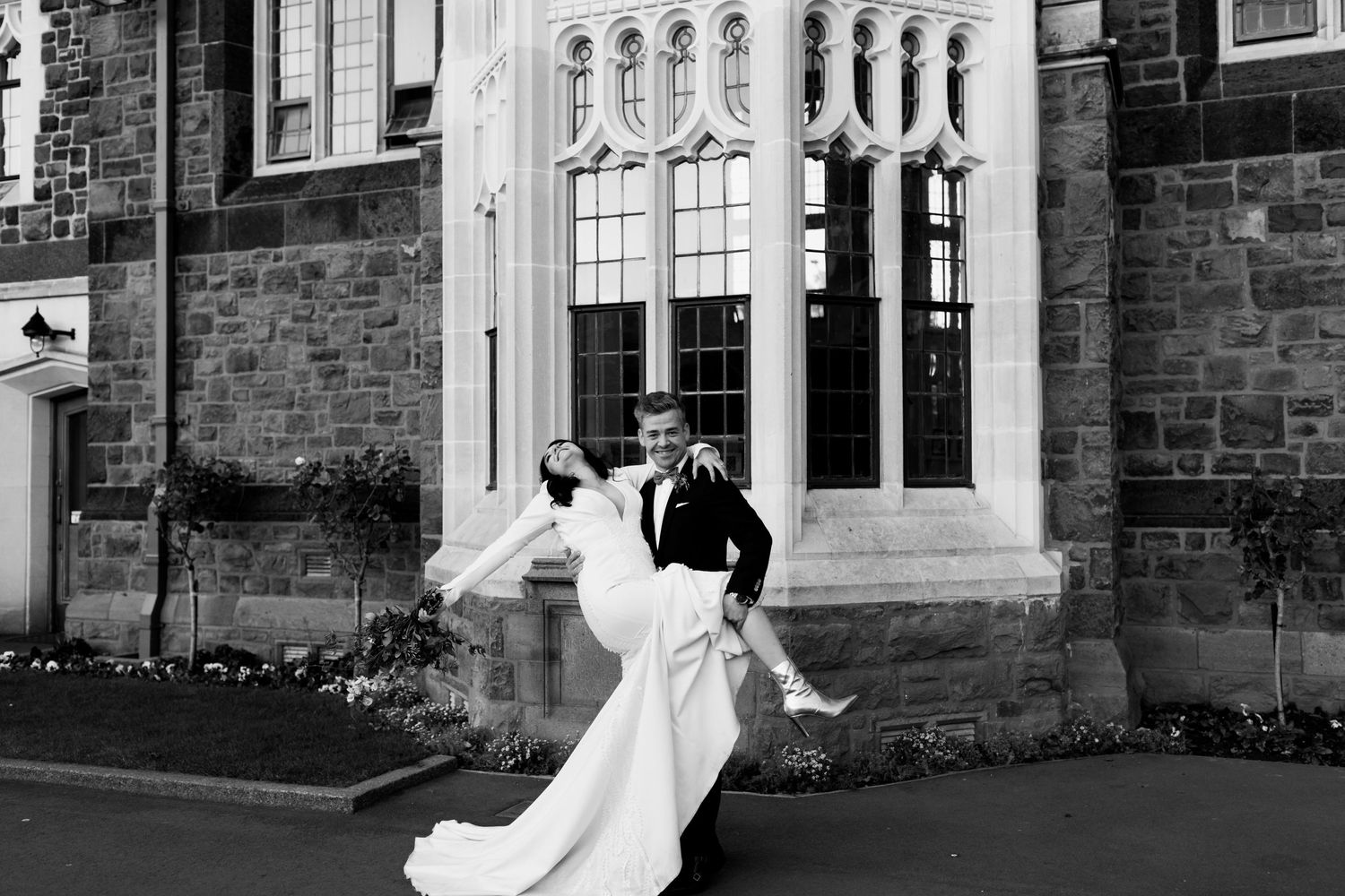 Black and white photo of dancing couple in wedding attire by stone building.