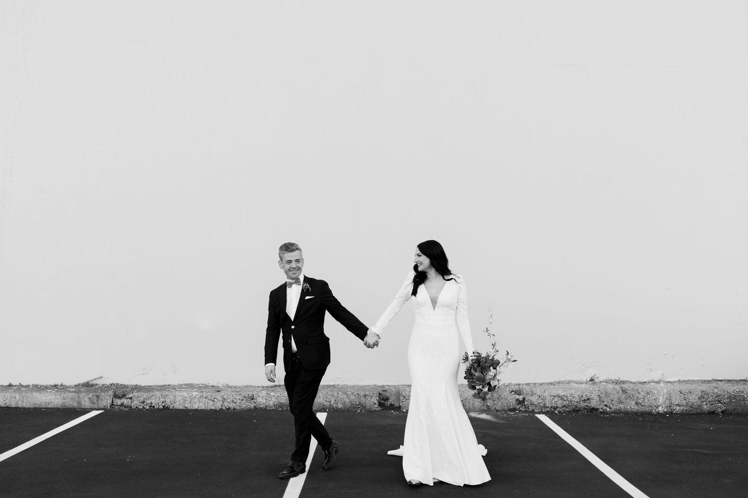 Black and white photo of couple walking hand in hand on parking lot lines.