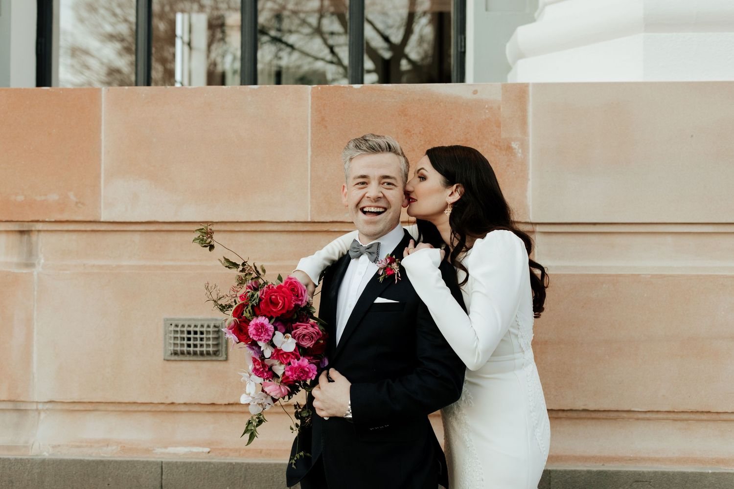 A joyful intimate moment between a couple in formal attire with bright pink florals.
