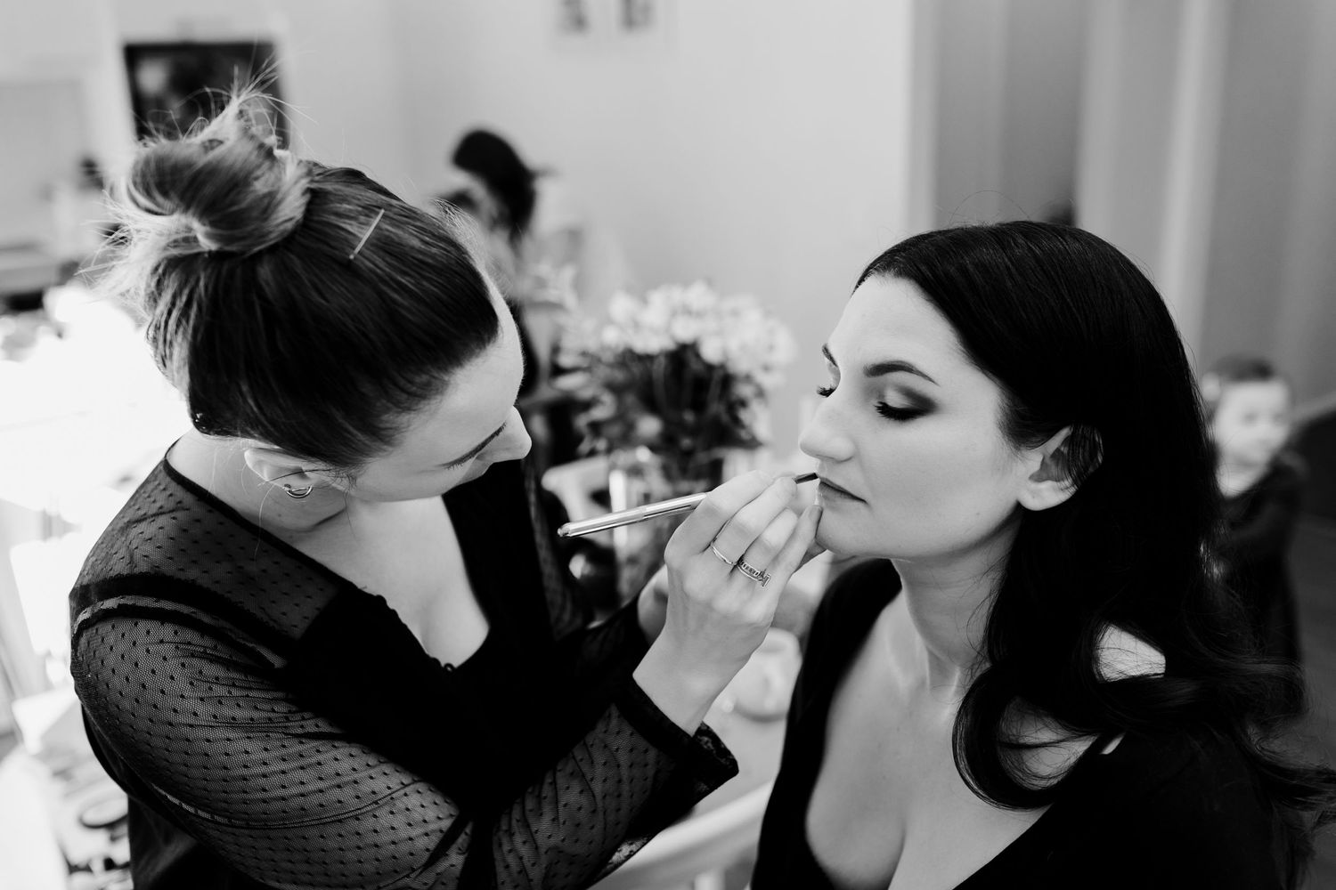 Black and white photo of makeup application during bridal preparation.