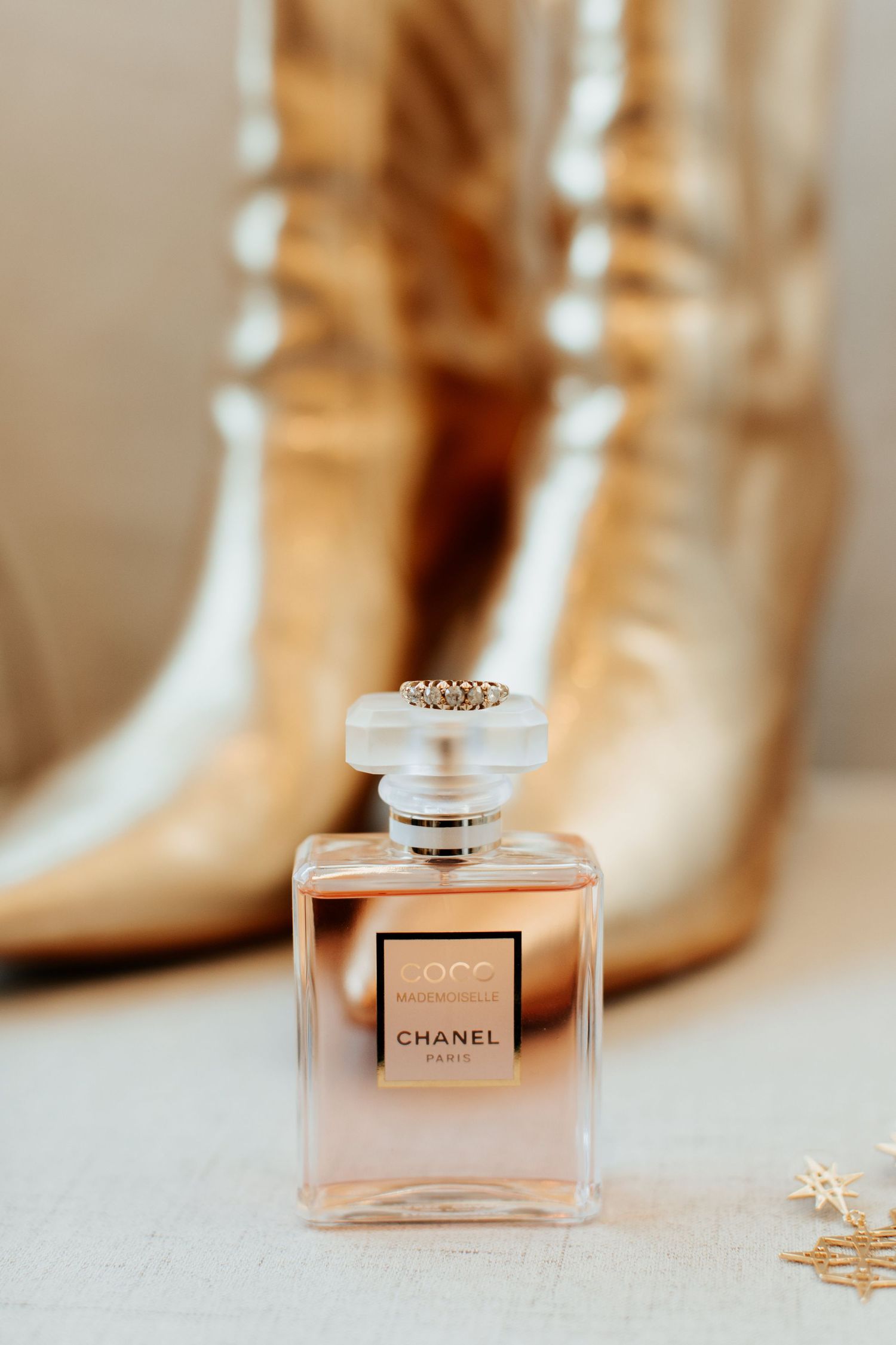 Chanel perfume bottle displayed with gold boots in soft focus background.