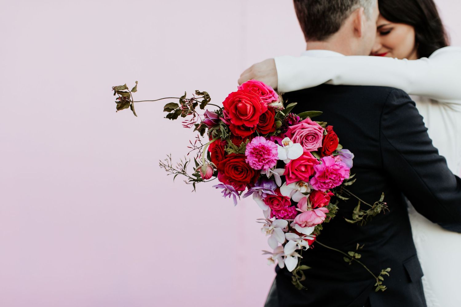 Close-up of vibrant pink and red wedding bouquet during couple's embrace.
