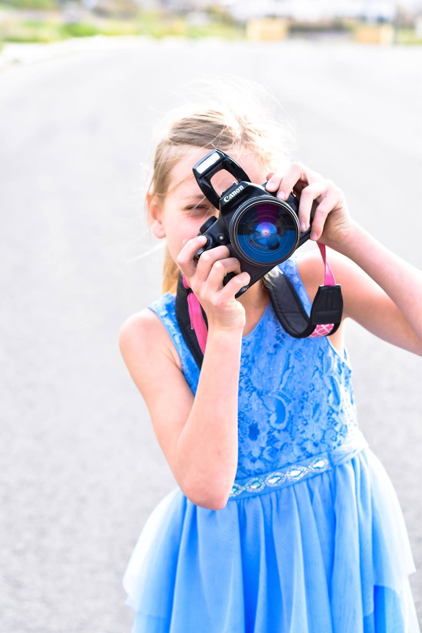 Young photographer in a blue dress holding a professional camera outdoors.