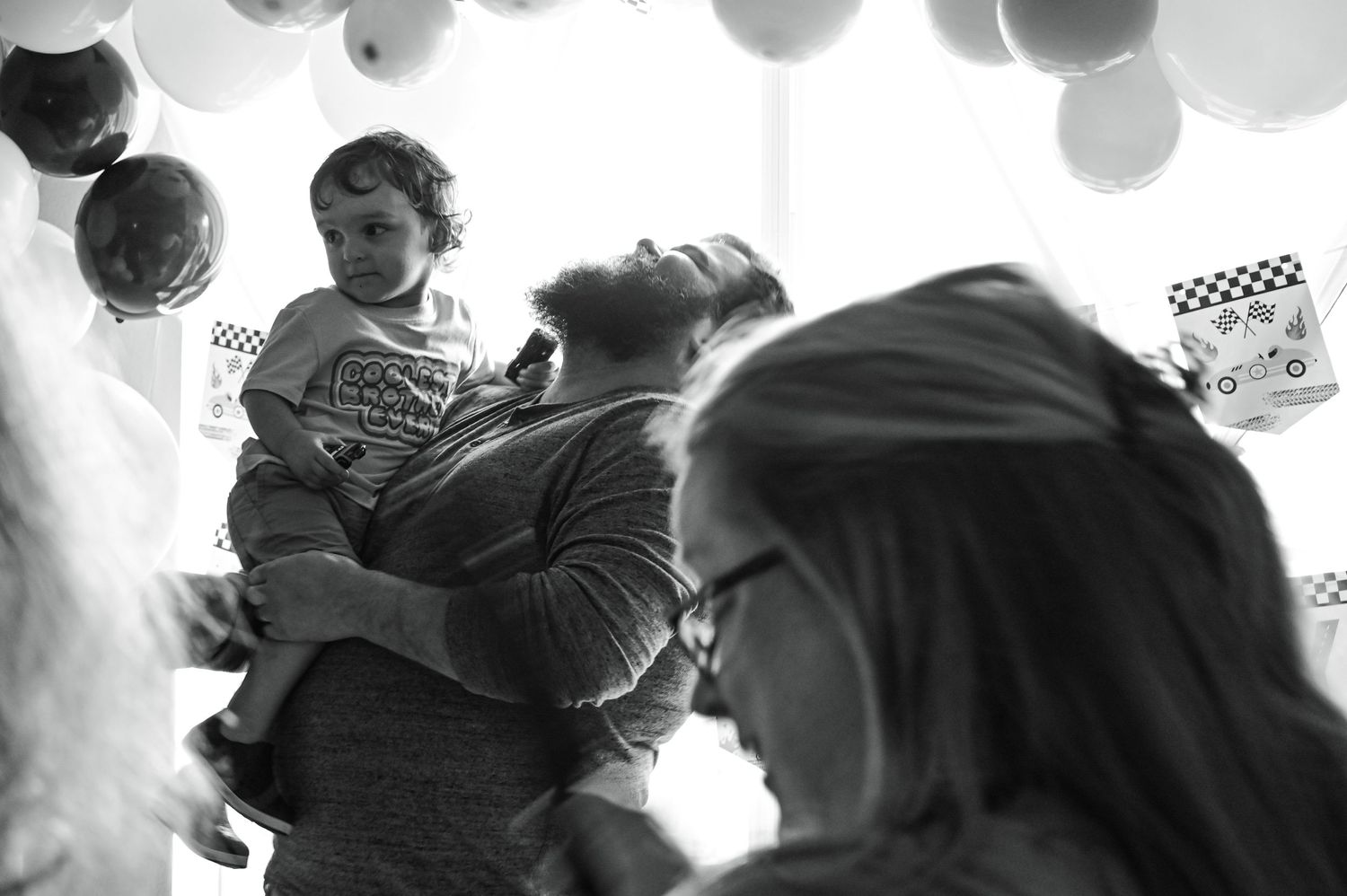 A black and white photo of a party scene with balloons and people gathered together.