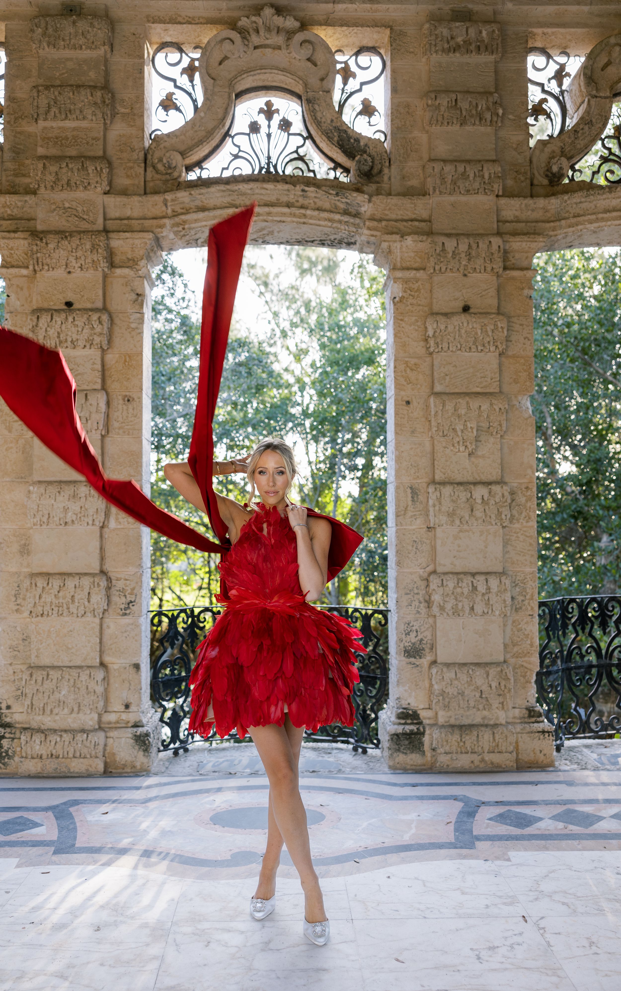 A flowing red dress twirls within historic stone colonnade architecture.