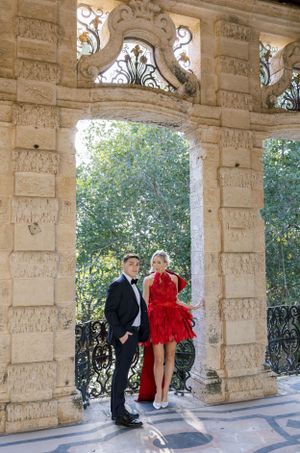 Couple poses under ornate stone archway with lush greenery in background.