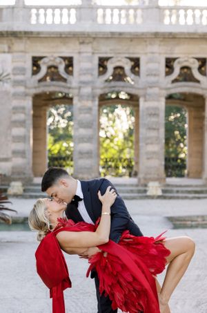 A romantic couple in formal attire share a dramatic dip pose in front of an elegant stone colonnade.