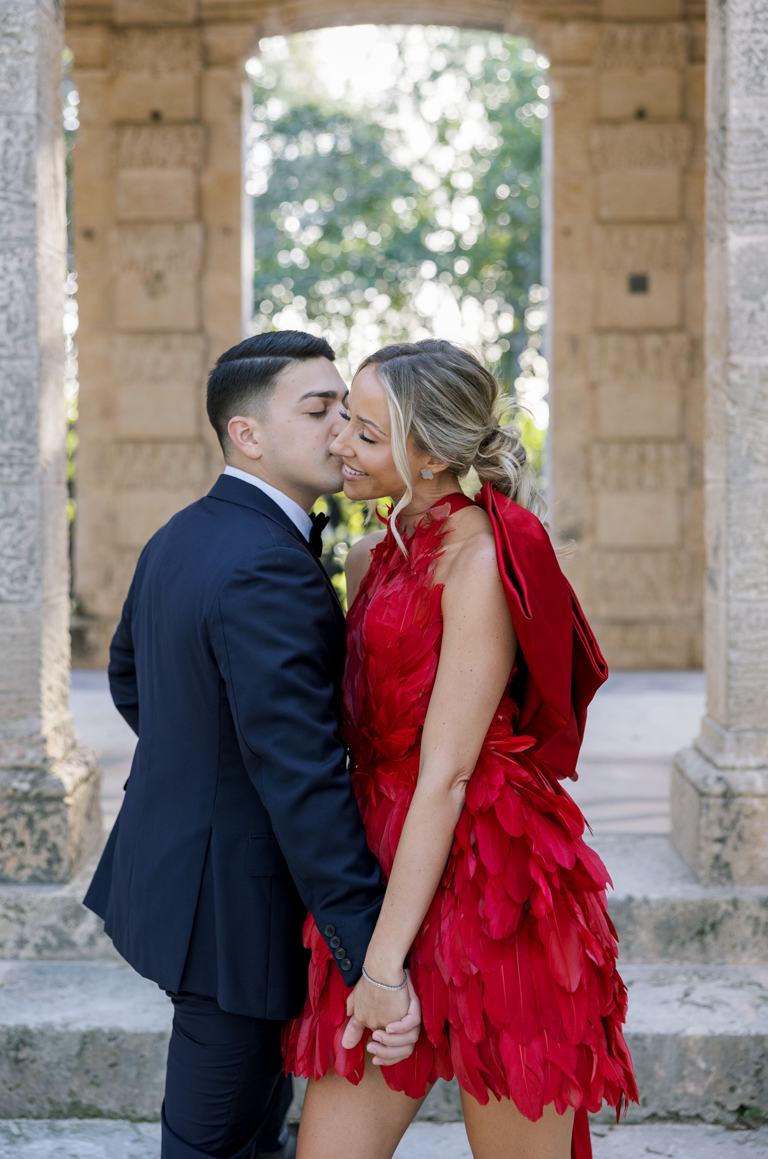 Intimate moment between couple wearing black suit and red feathered dress.
