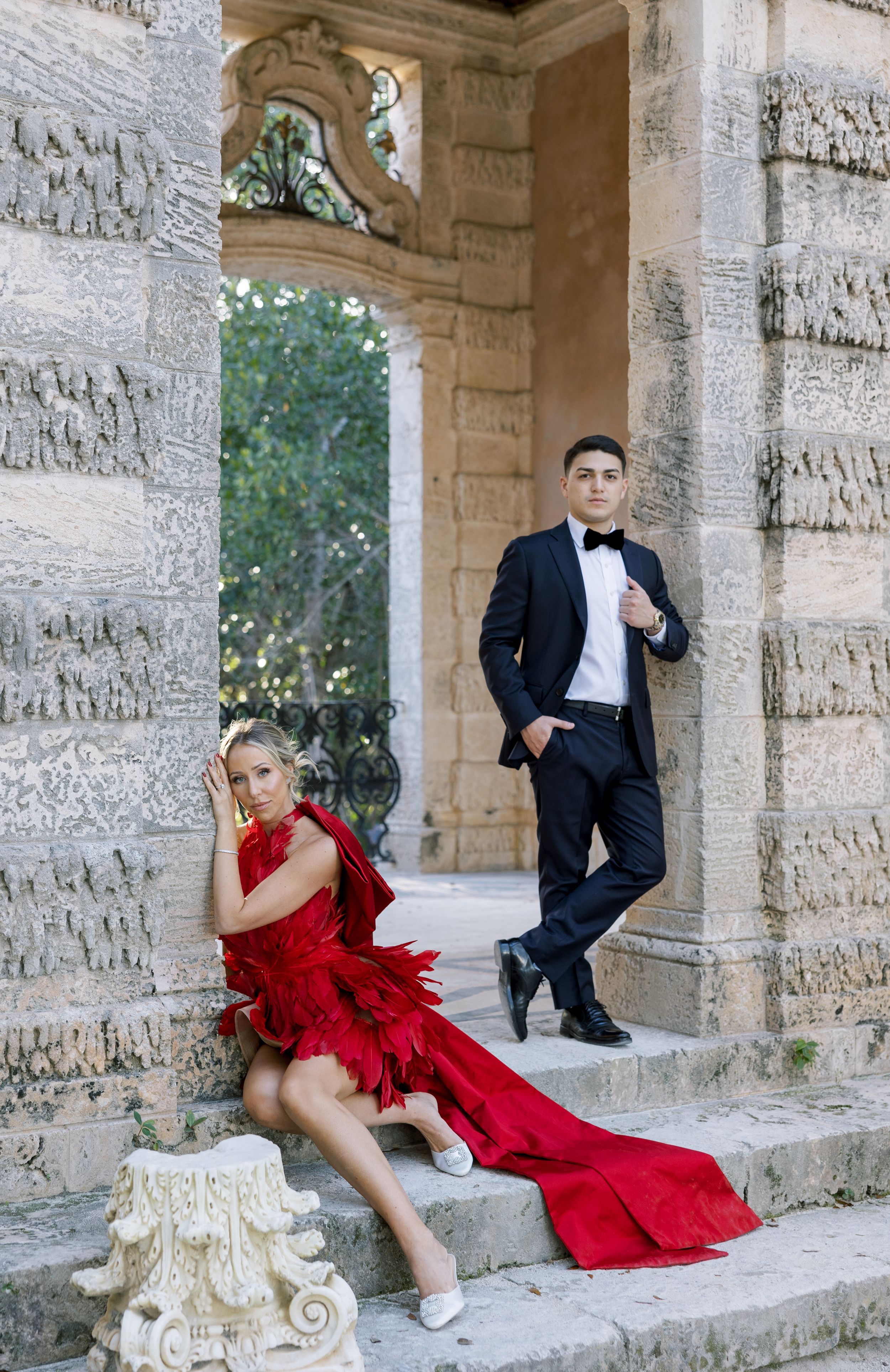 Dramatic fashion pose on stone steps of a classical building with ornate columns.