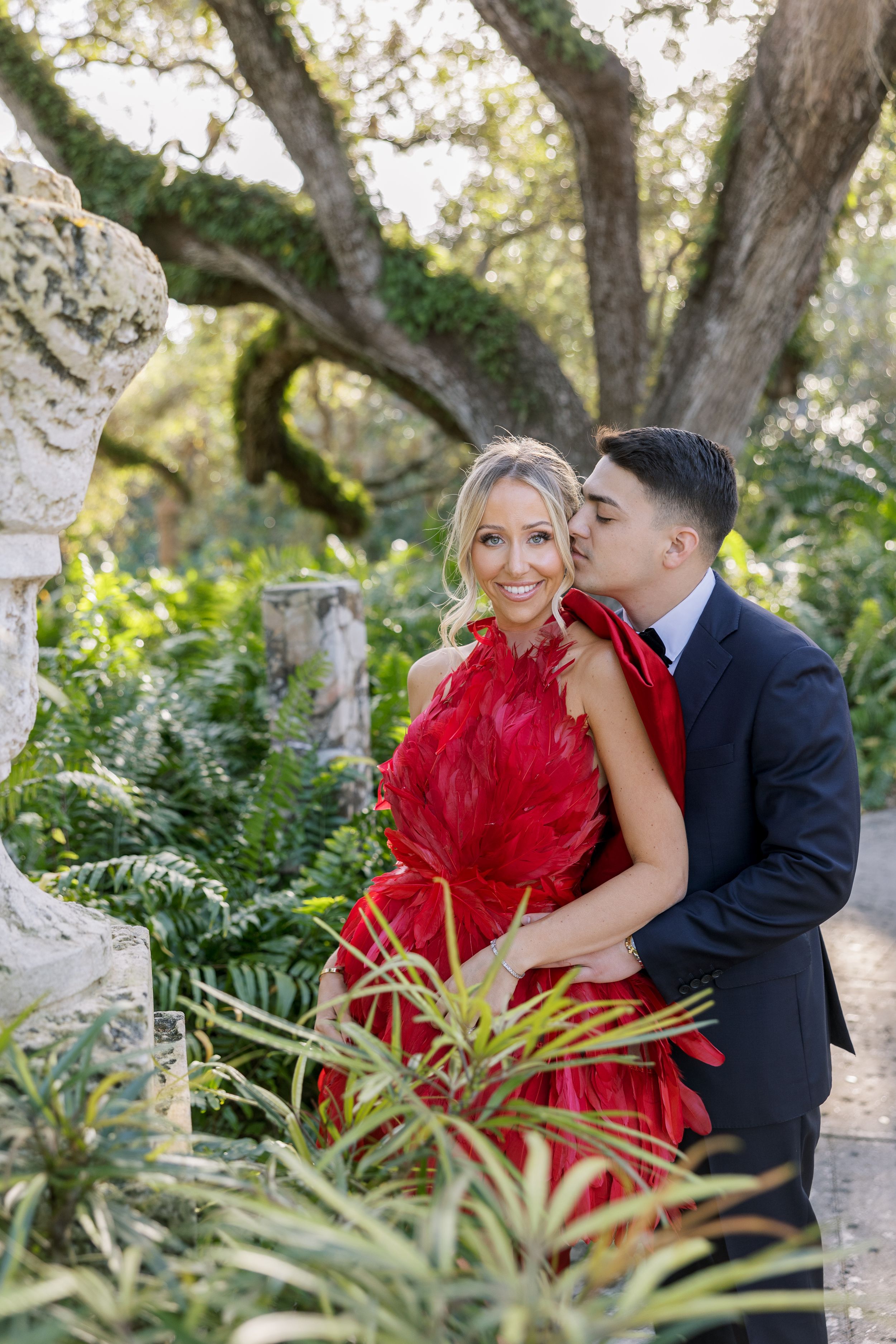 A couple shares a tender moment in a garden setting surrounded by tropical plants.