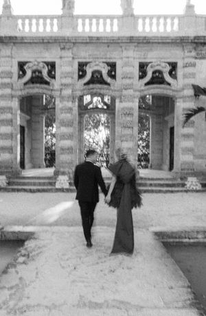 Black and white photo of couple walking towards ornate stone colonnade.