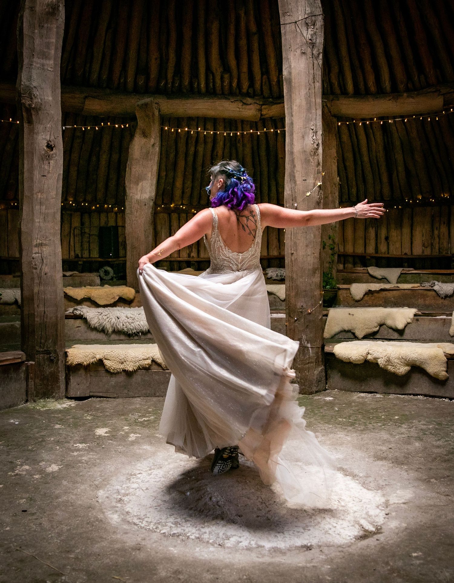 A dancer in a flowing white dress twirls gracefully inside a rustic wooden barn with string lights.