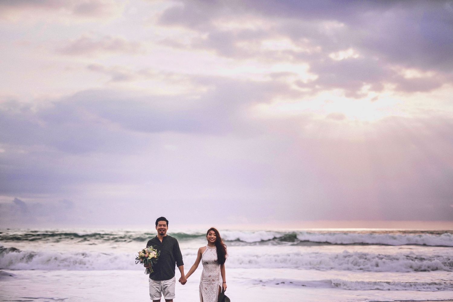Couple walking along a beach with crashing waves at sunset.