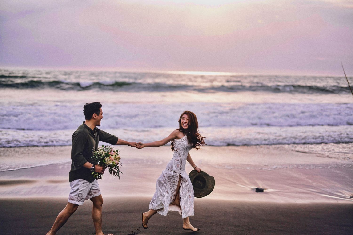 Playful couple running and dancing together along the shoreline during golden hour.