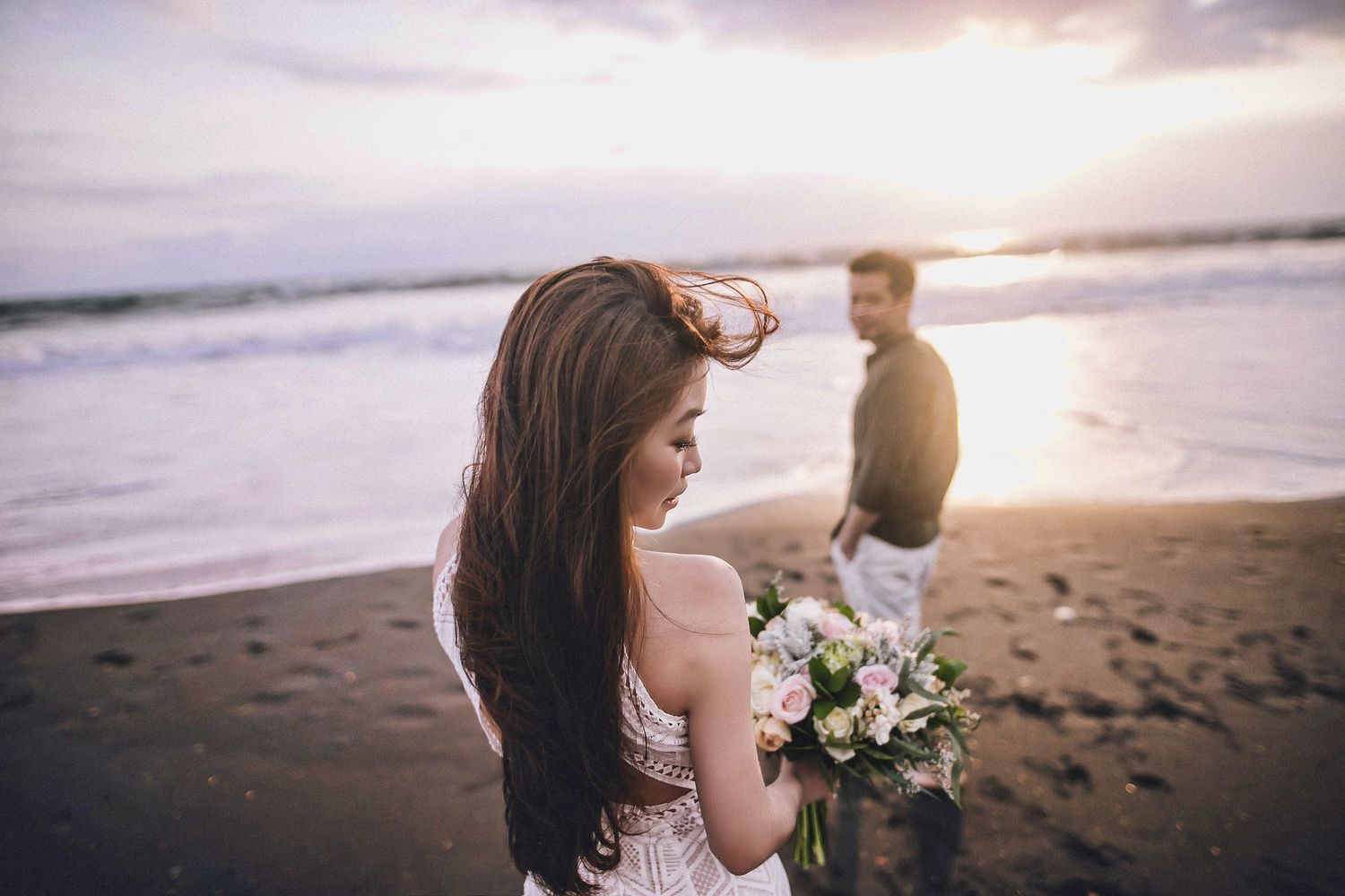 Couple walking along scenic beach with dramatic cliffs and sunset sky in background.
