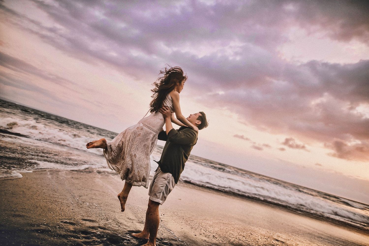 Couple dancing and playing together on sandy beach during golden hour.