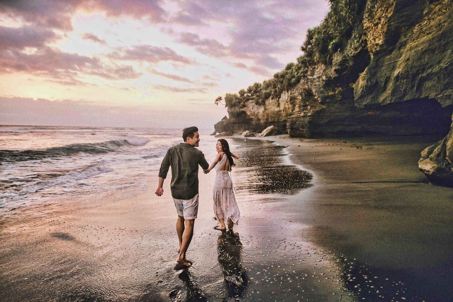 Couple walking hand in hand along dramatic coastal cliffs at sunset.
