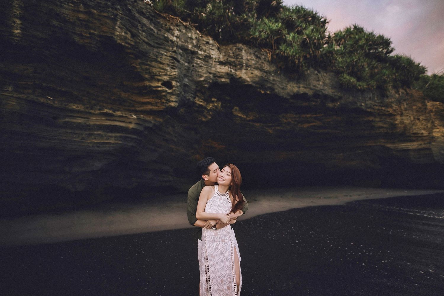 Couple in love poses against dramatic ocean cliffs during golden hour.