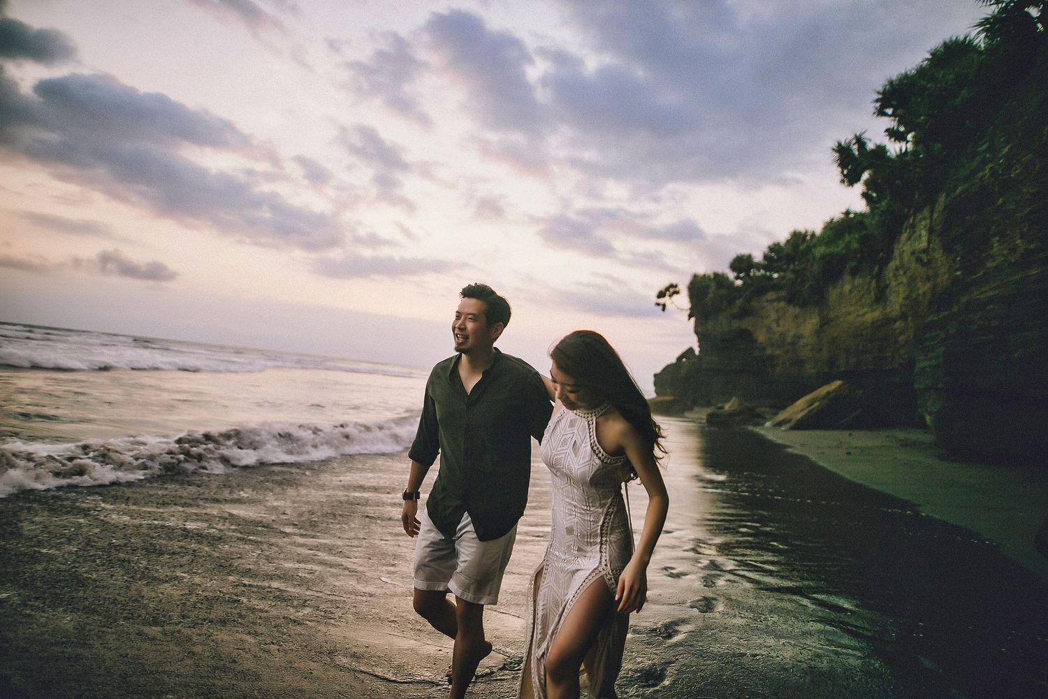 Couple enjoys romantic sunset moment on scenic beach with cliffs.
