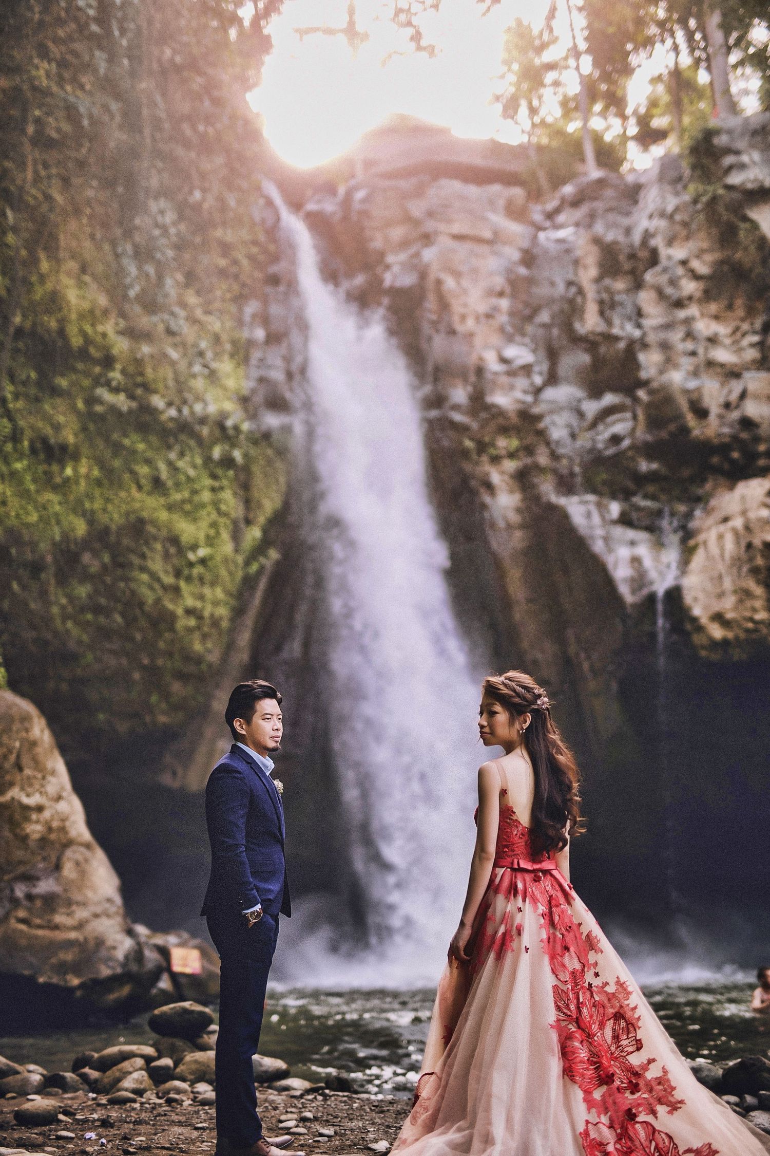 Couple poses in formal attire in front of majestic waterfall.