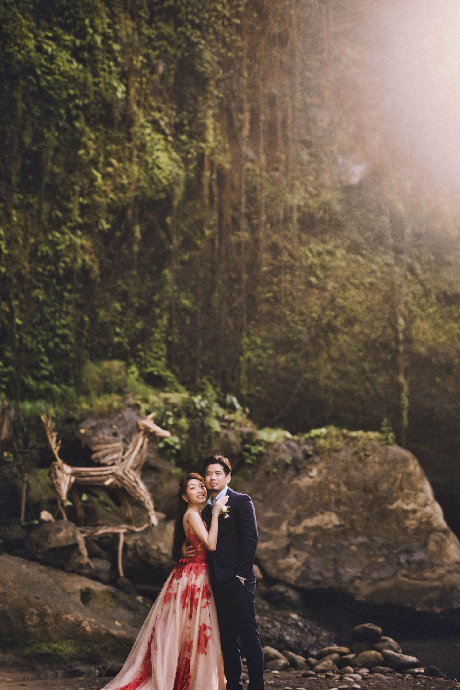 Couple in formal wear dances near misty waterfall in romantic setting.