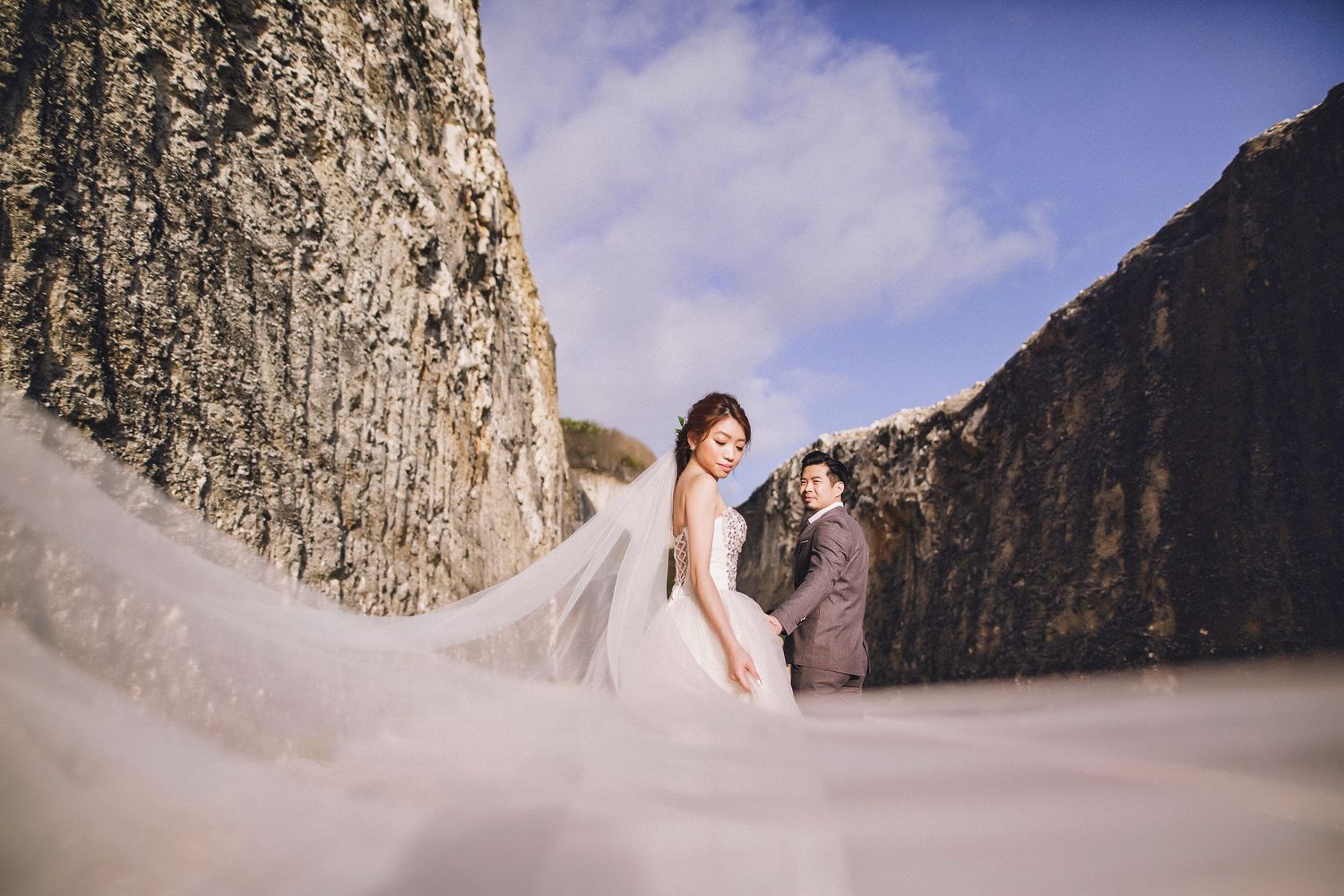 Couple poses along a rugged coastal path with dramatic cliffs and ocean views.