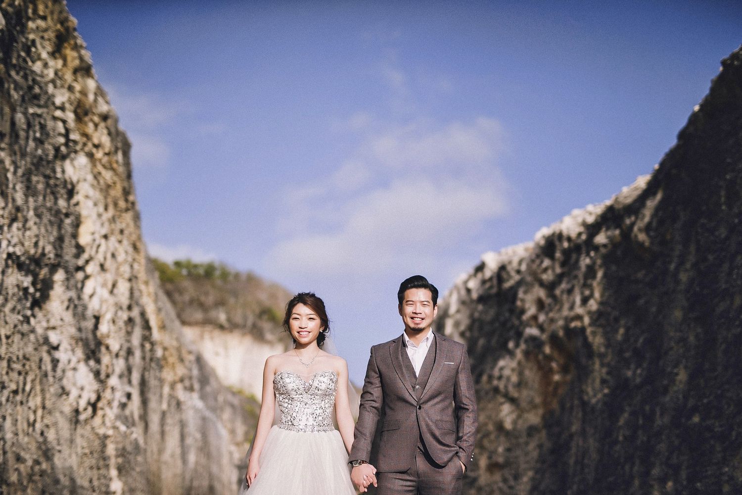Dramatic wedding portrait against towering rocky cliffs and blue sky in a scenic outdoor location.