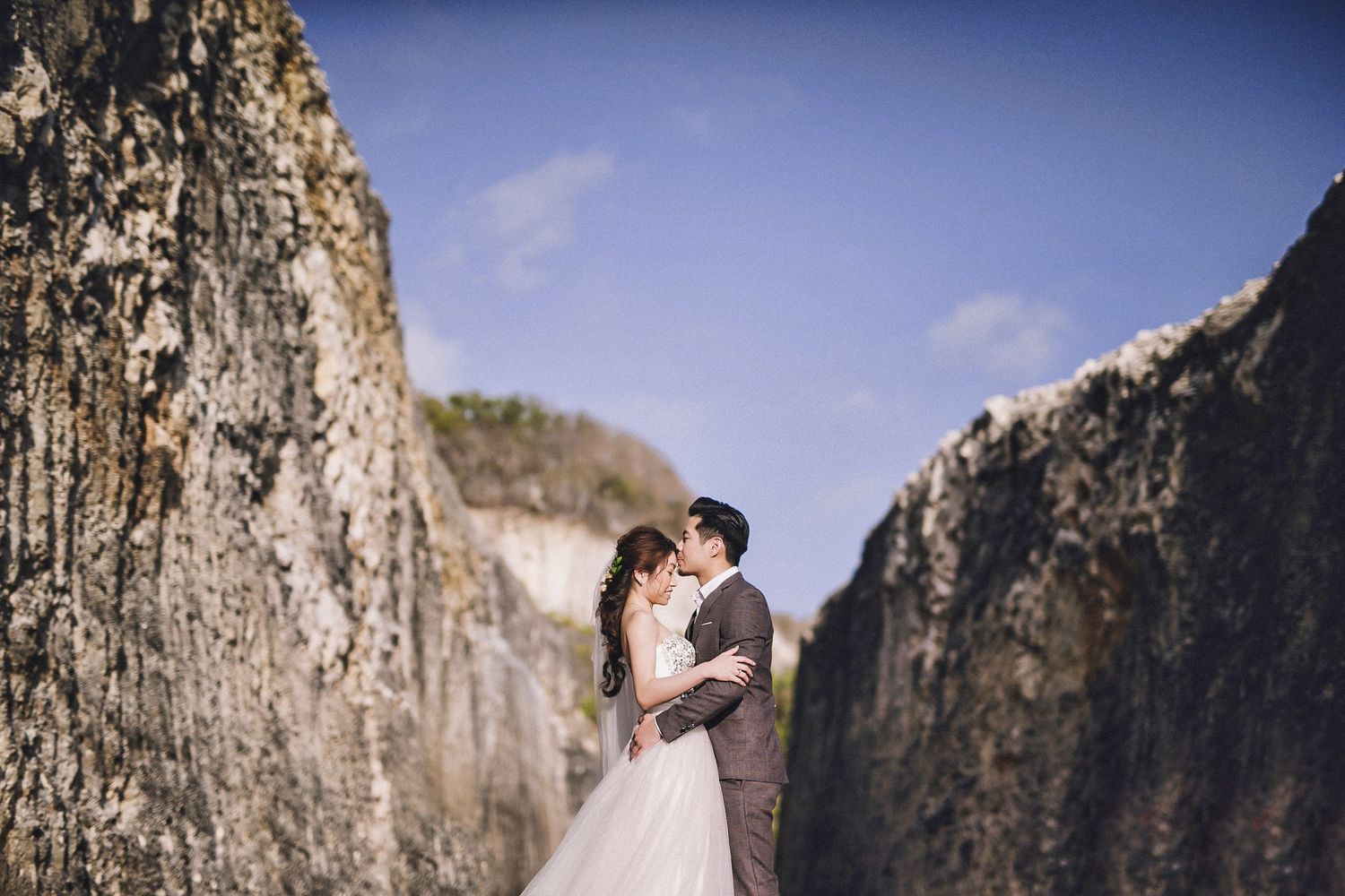 Wedding couple embracing on scenic mountain path surrounded by towering cliffs.