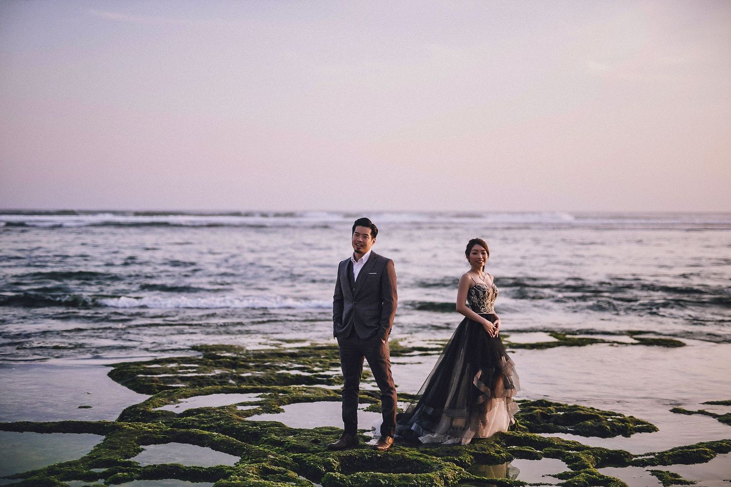Romantic sunset beach wedding photography with mossy rocks and ocean waves.