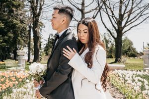 Bride hugging Groom from behind in front of beautiful flowers