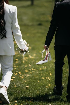 Groom and Bride walking together while holding flowers and heels