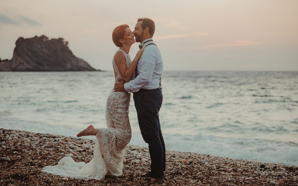 Love is in the air as the bride and groom embrace for a tender kiss on the beach, with the sun setting behind them.