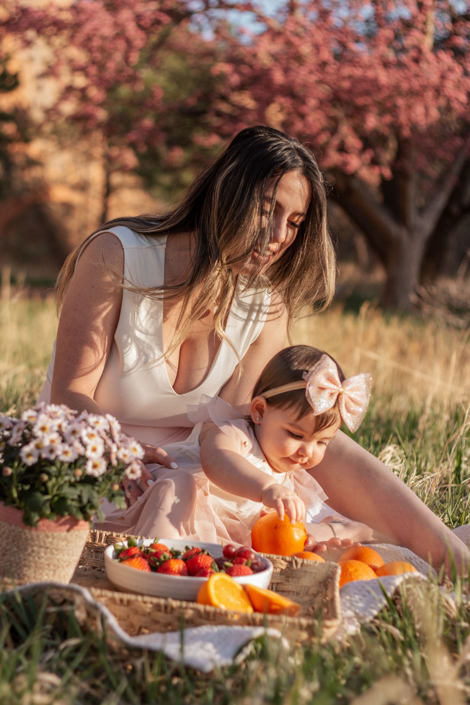 Mother and daughter having a picnic outdoors with fresh fruits amid pink blossoming trees during golden hour. Colorado, family photoshoot