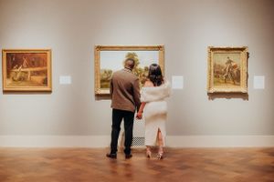 Art gallery interior with multiple framed paintings displayed on beige walls.