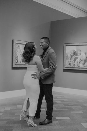 Two people share an intimate moment while viewing art in a minimalist gallery space.