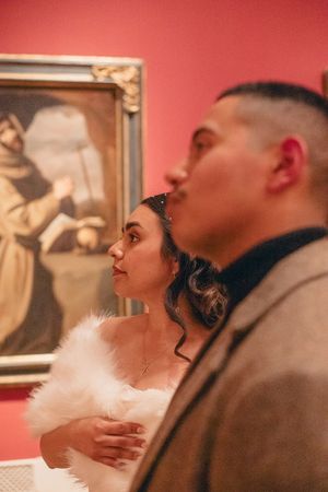 Couple gazes at artwork on red gallery walls during what appears to be a romantic museum date.