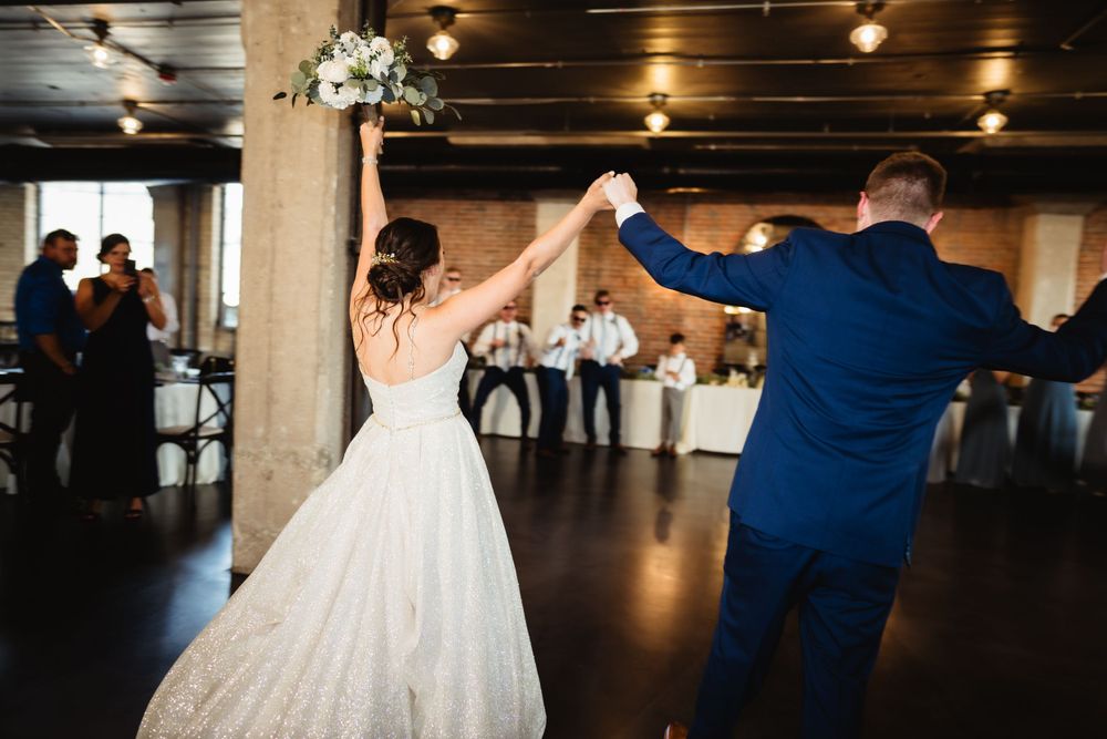 Newlyweds spinning and dancing together on wooden floor at reception venue.