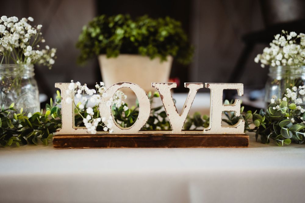 Illuminated white LOVE sign display with greenery and flowers as wedding decor on table.