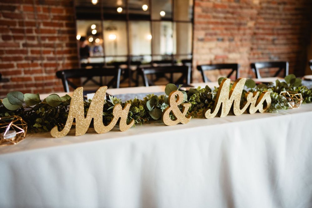 Gold Mr & Mrs sign decorating head table with greenery garland at wedding reception.