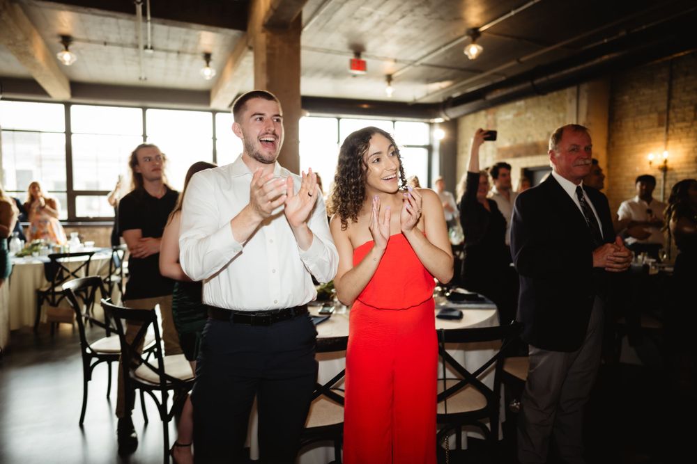 Wedding guests clapping and celebrating during reception at indoor venue.