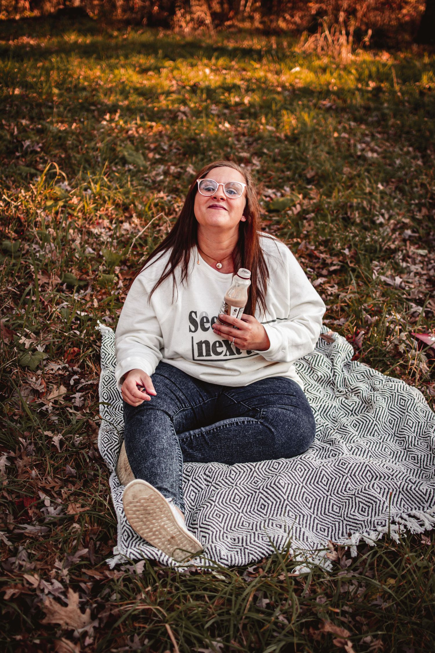 Person relaxing on patterned blanket in autumn woods with warm sunset lighting.