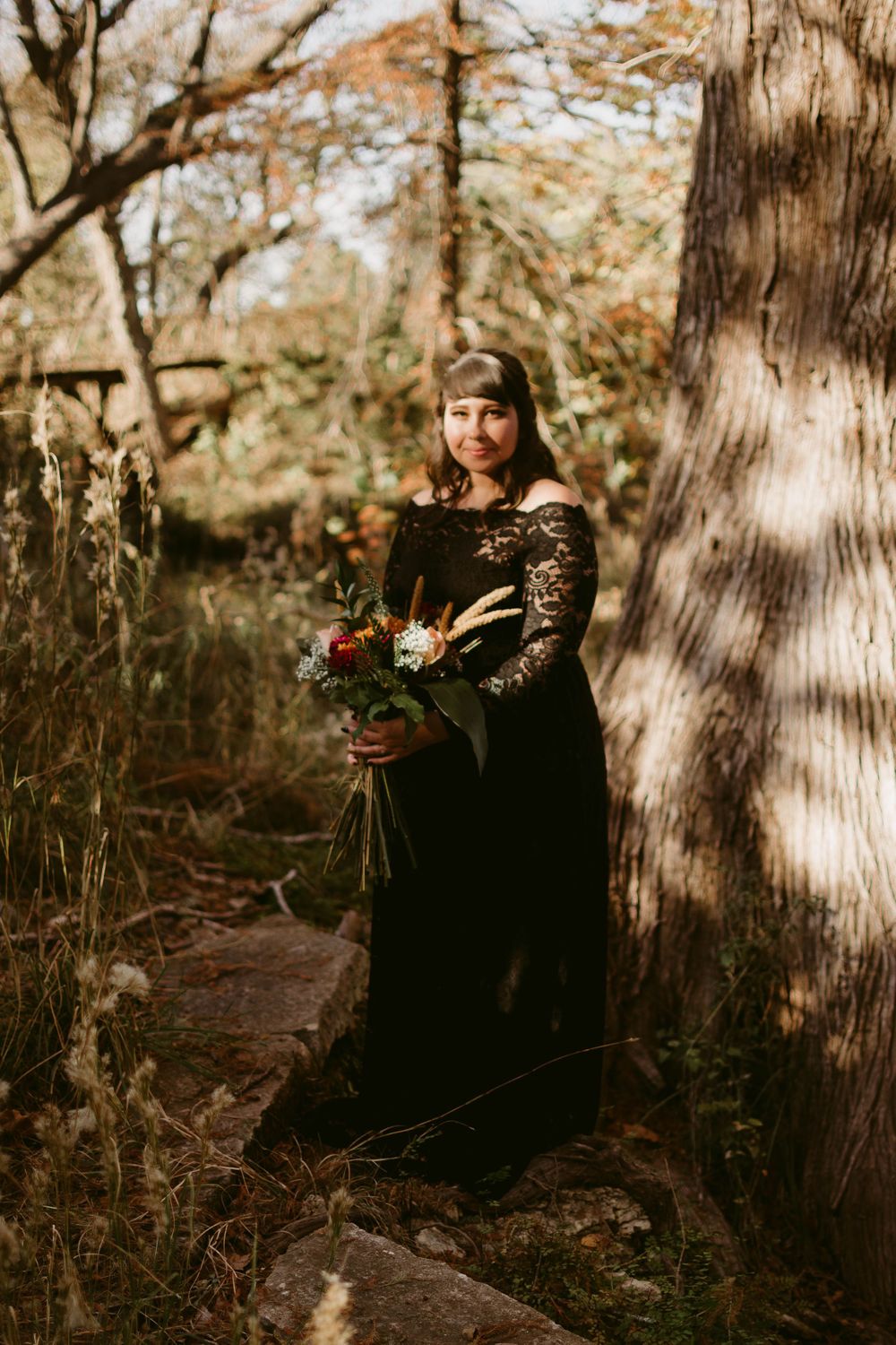 A romantic forest scene with someone holding a red bouquet while wearing a black lace dress.