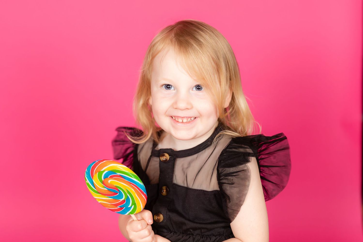 little girl child in black dress with bright lollipop on tulip pink savage backdrop in studio in clayton new jersey