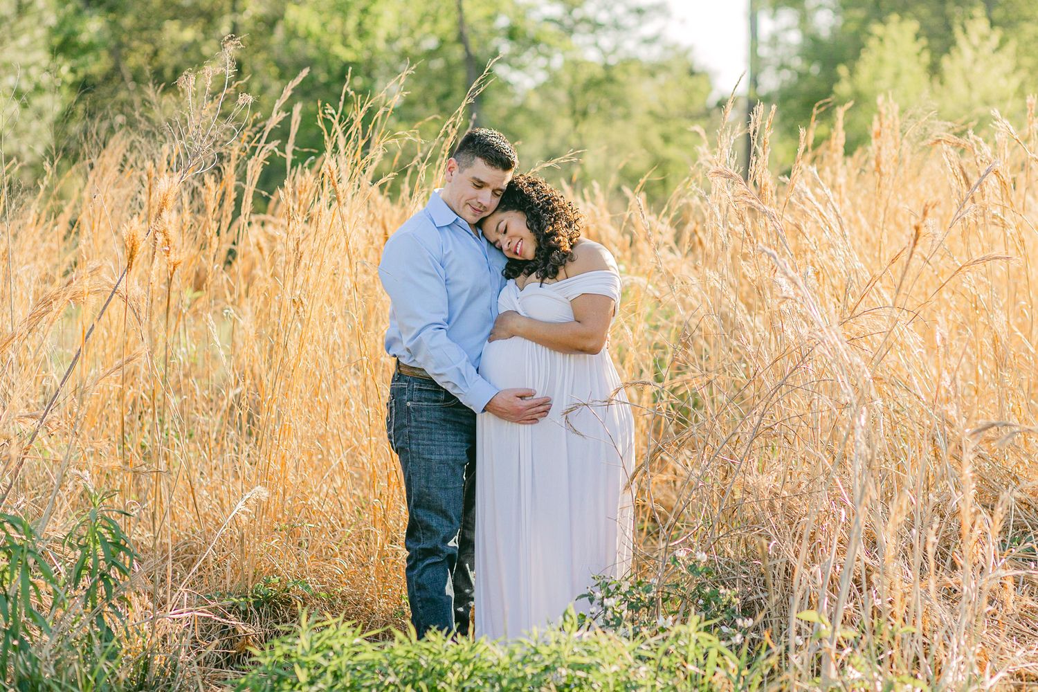 A pregnant woman lays her head on her husband's chest as he cradles her baby bump.
